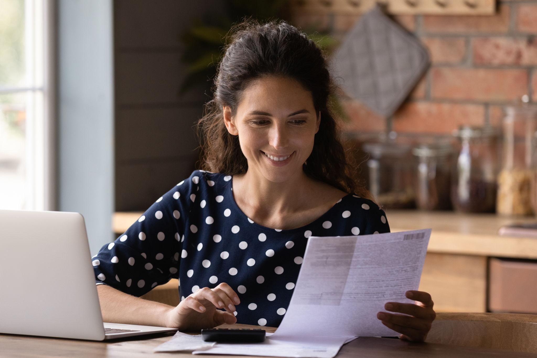 Smiling woman checking financial documents, calculating bills, using laptop